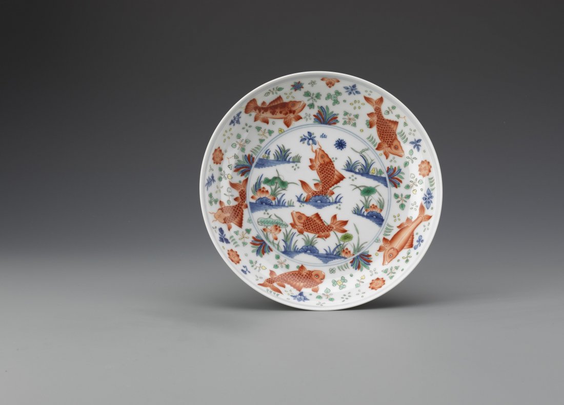 Chinese Doucai 'Fish' Dish: A rare fine painted doucai 'fish' dish, painted in the centre with iron-red carps, one leaping from the water, in a river pool with lotus and arrow-weed, in green, yellow and iron-red enamels with lig