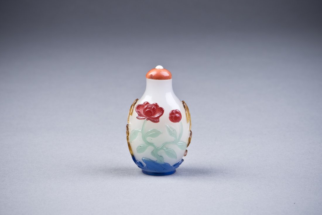 Peking Snuff Bottle: A Peking Glass Snuff Bottle of Bulbous form, with colorful relief overlay, featuring lotus flowers and butterfly elements, and a coral color design cap. Height 2.25 Diameter 1.5''