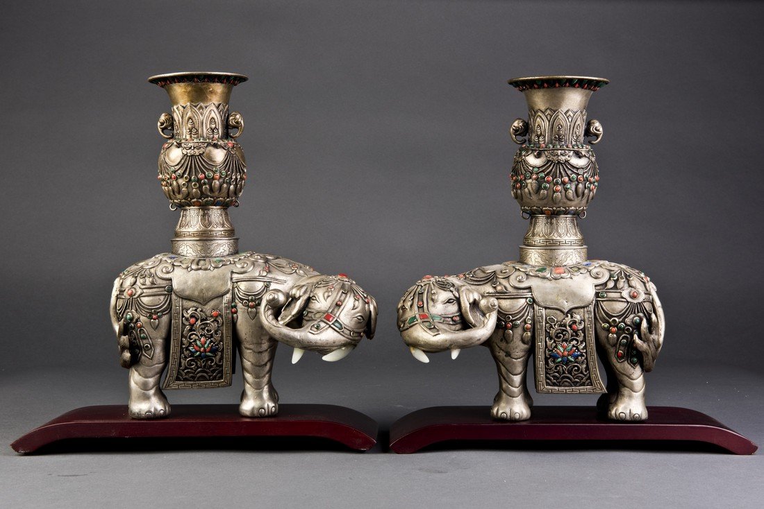 A Pair of Silver Elephant Statue: Two standing silver elephants each carrying a silver vase on the back and turning their heads raised to the side. The intricate deep relief details and decorative blue and red beads attributed to the 
