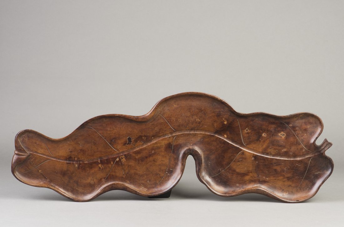A ROSEWOOD TEA TRAY: A hardwood tea tray designed in the form of an elongated and curved leaf with the incisement of vein on the recessed front side. Height 0.5" Length 21.5" Width 7"