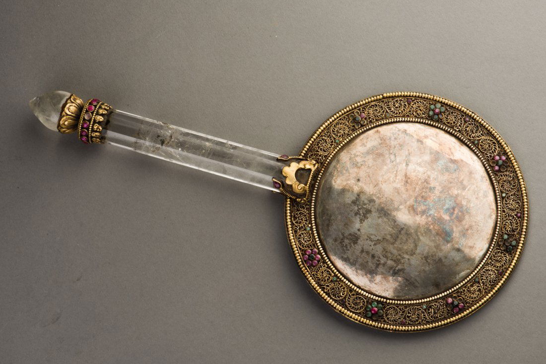 A FILIGREE BRONZE MIRROR WITH CRYSTAL HANDLE: The archaistic round bronze mirror features intricate decoration around the rim on one side and patina around a roundel of lucky character, a translucent handle with matching bronze motif. Height 12.5