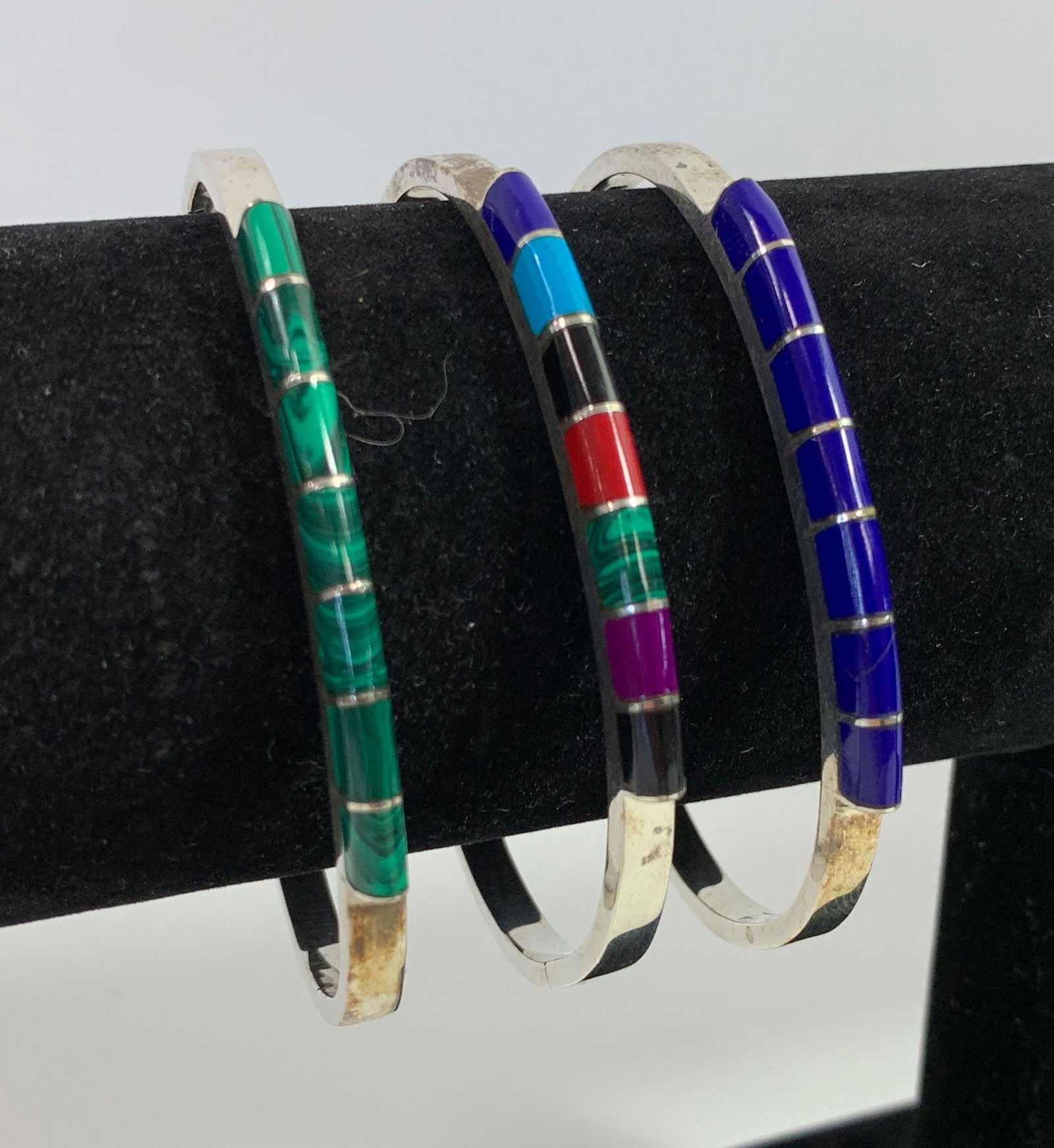 THREE STERLING AND STONE CUFFS: THREE STERLING AND STONE CUFFS ~ MEXICO MADE. MATCHED SET. 2.625" IN DIAMETER. HINGED. INLAID W/AZURITE, MALACHITE, SUGILITE, ONYX, AND TURQUOISE STONES. 2.02 TROY OUNCES TW.