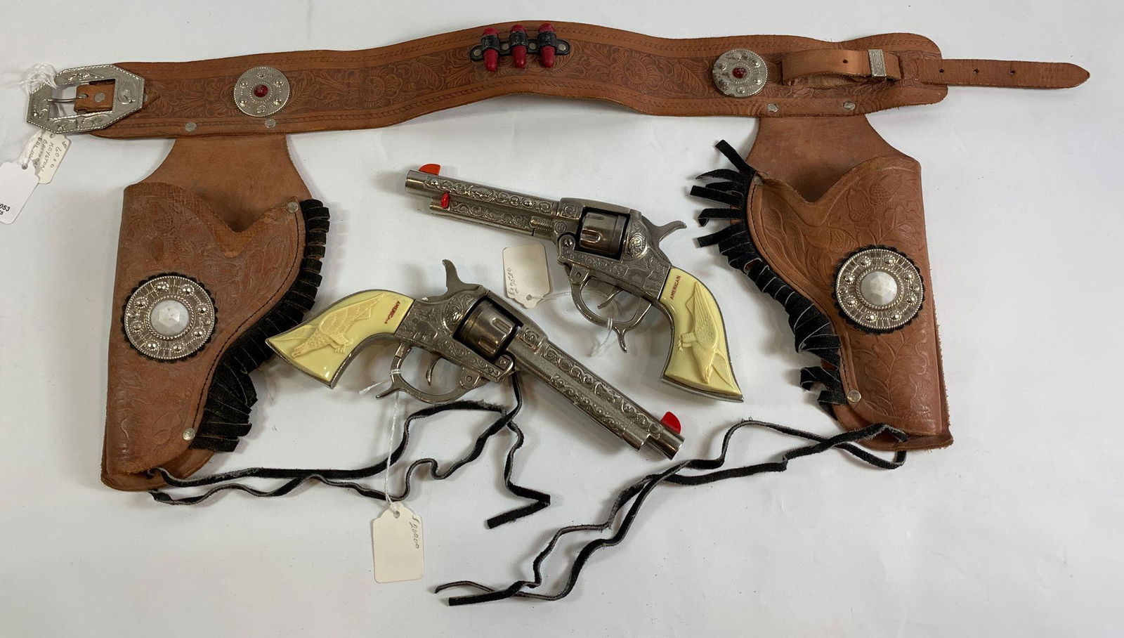 BROWN LEATHER DOUBLE HOLSTER SET WITH BULLETS, RED &: BROWN LEATHER DOUBLE HOLSTER SET WITH BULLETS, RED & WHITE JEWELS AND BLACK FRINGE AND PAIR OF 1940's KILGORE "AMERICAN" CAST IRON CAP GUNS WITH FLYING EAGLE GRIPS