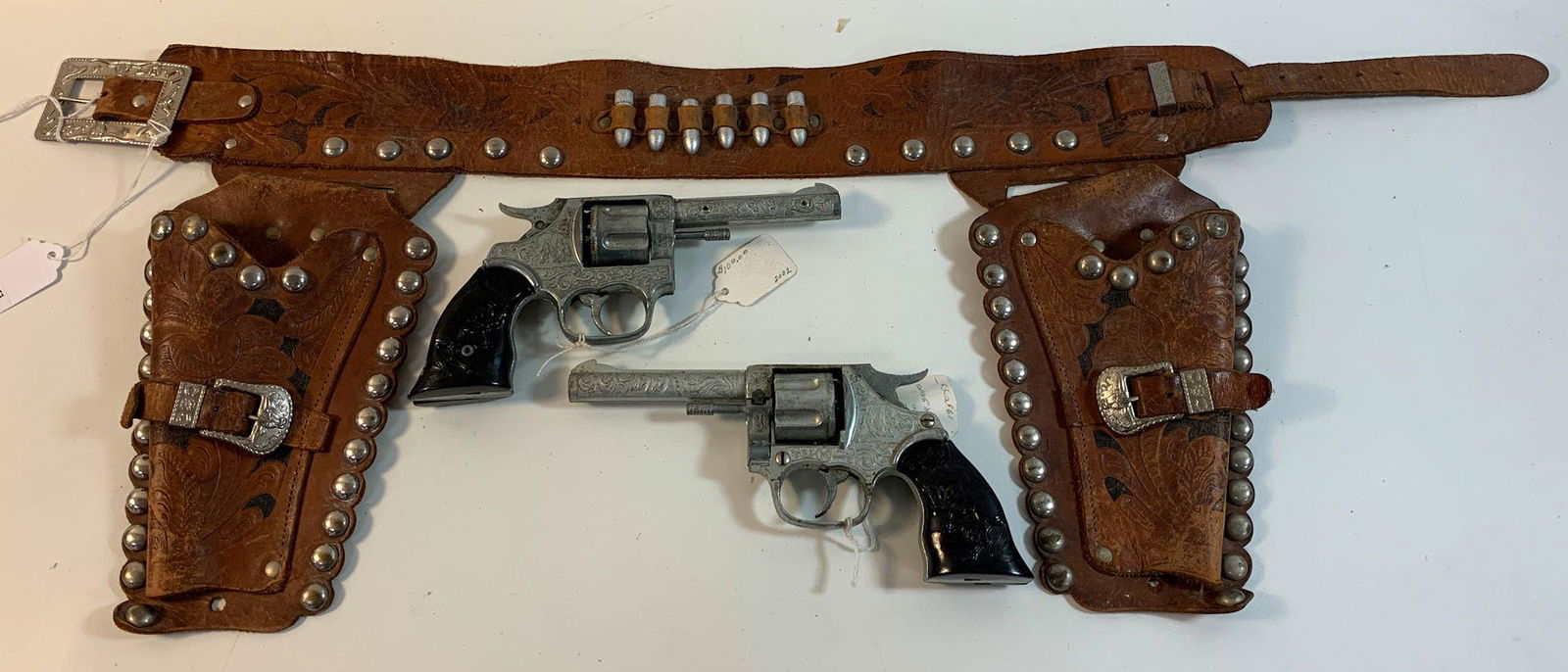 BROWN LEATHER DOUBLE HOLSTER SET WITH METAL STUDS AND: BROWN LEATHER DOUBLE HOLSTER SET WITH METAL STUDS AND SILVER BULLETS AND PAIR 1950's KILGORE "BRONCO" CAP GUNS WITH BLACK BUCKING HORSE GRIPS