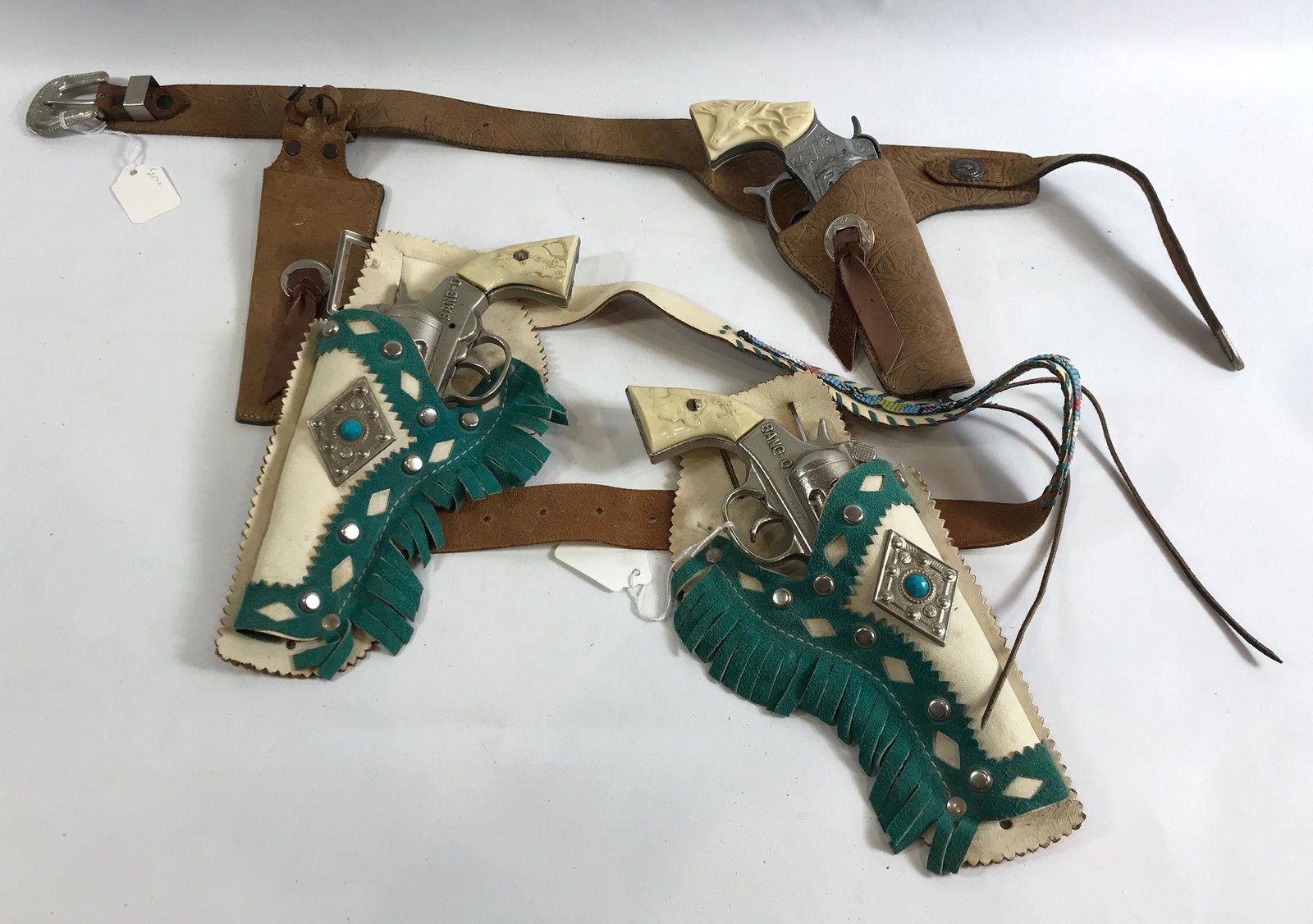 BROWN LEATHER HOLSTER AND KNIFE SHEATH WITH KILGORE CAP: BROWN LEATHER HOLSTER AND KNIFE SHEATH WITH KILGORE CAP GUN AND WHITE LEATHER DOUBLE HOLSTER WITH BLUE FRINGE AND BEADED BELT WITH 1938-1940 BANG-O CAST IRON GUNS WITH HORSEHEAD GRIPS