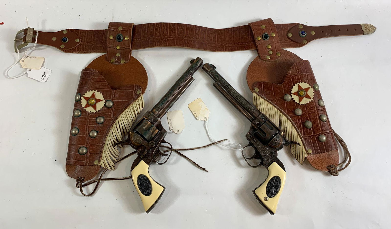 PAIR OF 1950's L-H MARSHALL (HALCO) CAP GUNS WITH: PAIR OF 1950's L-H MARSHALL (HALCO) CAP GUNS WITH COPPER FINISH, FLOWER OVAL GRIPS AND BROWN DOUBLE HOLSTER WITH WHITE FRINGE, STUDS AND JEWELS