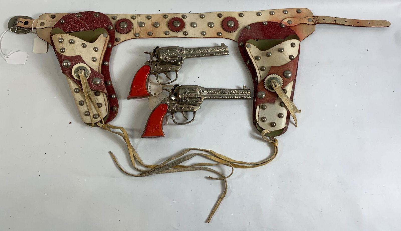 RED AND WHITE LEATHER DOUBLE HOLSTER SET WITH STUDS AND: RED AND WHITE LEATHER DOUBLE HOLSTER SET WITH STUDS AND FRINGE AND PAIR OF KILGORE 1940's CAST IRON "RANGER" CAP GUNS WITH RED GRIPS