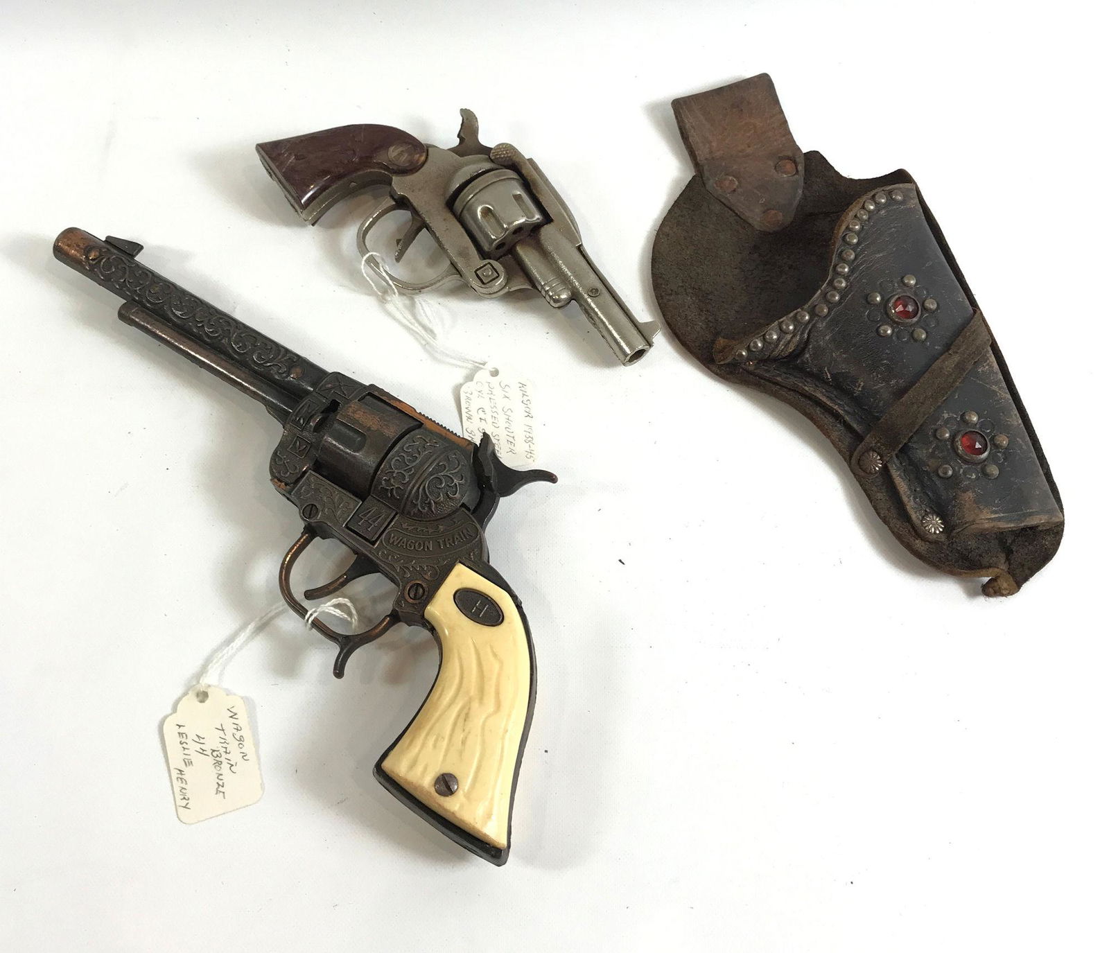 VINTAGE LESLIE HENRY BRONZE WAGON TRAIN 44 TOY CAP GUN: VINTAGE LESLIE HENRY BRONZE WAGON TRAIN 44 TOY CAP GUN AND 1940's KILGORE SIX SHOOTER PRESSED STEEL REVOLVING CYLINDER CAP GUN WITH BROWN HORSE GRIPS AND BROWN LEATHER HOLSTER WITH RED JEWEL AND STUDS