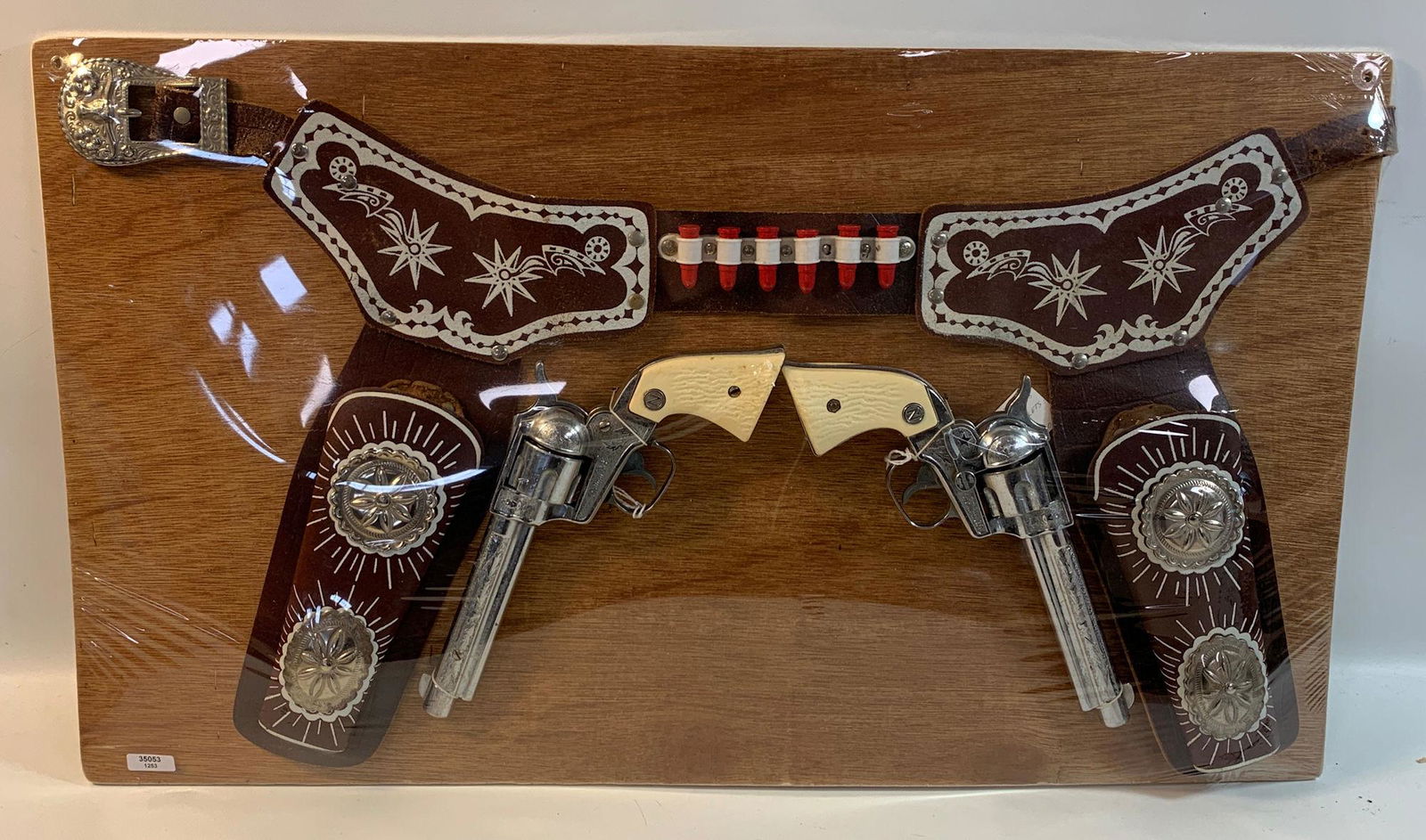 BROWN LEATHER DOUBLE HOLSTER SET WITH RED BULLETS,: BROWN LEATHER DOUBLE HOLSTER SET WITH RED BULLETS, WHITE DECORATION AND SILVER CONCHOS AND PAIR OF NICHOLS STALLION 38 REVOLVER CAP GUNS, DISPLAYED ON BOARD