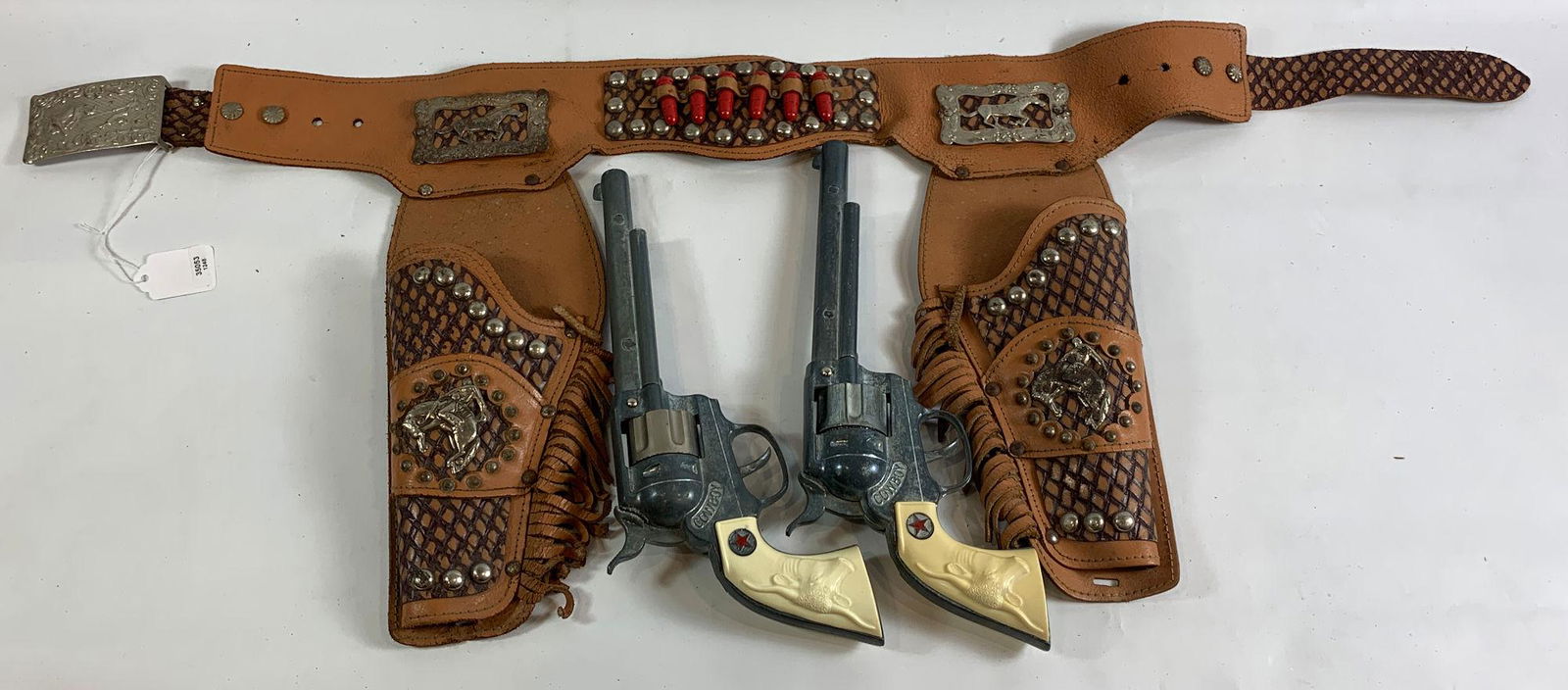 BROWN LEATHER DOUBLE HOLSTER SET WITH RED BULLETS,: BROWN LEATHER DOUBLE HOLSTER SET WITH RED BULLETS, SILVER STUDS, COWBOY CONCHOS, FRINGE AND PAIR OF "COWBOY" CAP GUNS WITH STEER HEAD GRIPS