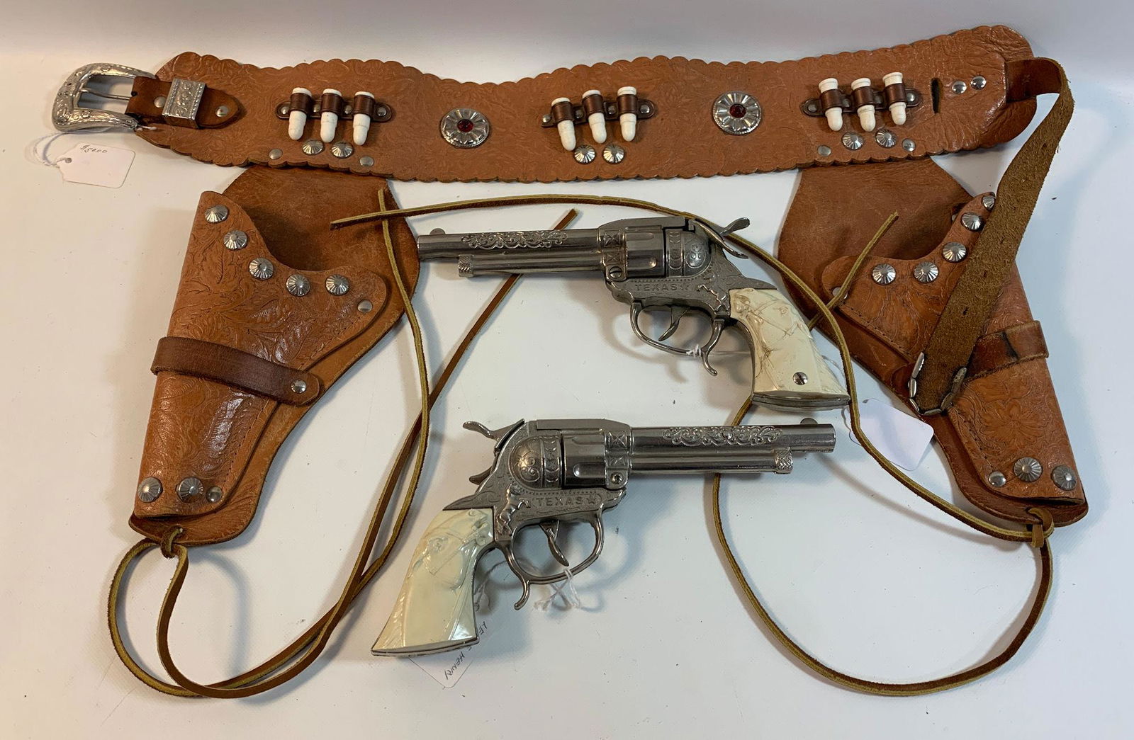 TAN LEATHER DOUBLE HOLSTER WITH METAL STUDS AND BULLETS: TAN LEATHER DOUBLE HOLSTER WITH METAL STUDS AND BULLETS AND PAIR OF LESLIE HENRY "TEXAS" CAP GUNS WITH MOLDED PLASTIC HORSEHEAD GRIPS