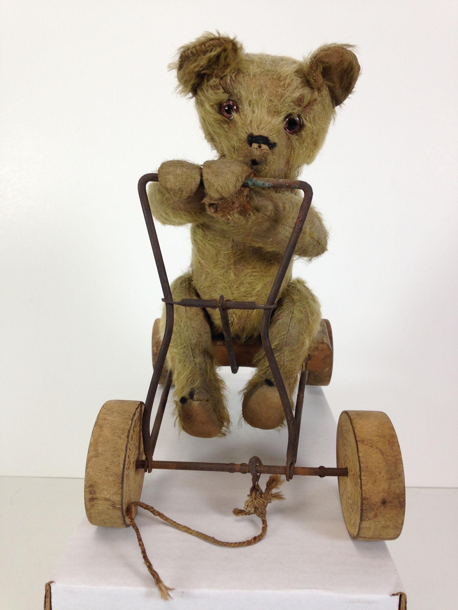 VINTAGE TEDDY BEAR PULL TOY. CARAMEL MOHAIR, APPLIED: VINTAGE TEDDY BEAR PULL TOY. CARAMEL MOHAIR, APPLIED EARS, GLASS EYES, ON PIN JOINTED BODY, ATTACHED TO A METAL AND WOOD CART. WHEN PULLED, THE BEAR "ROWS" BACK AND FORTH. WHEELS ARE INCISED "BRITISH