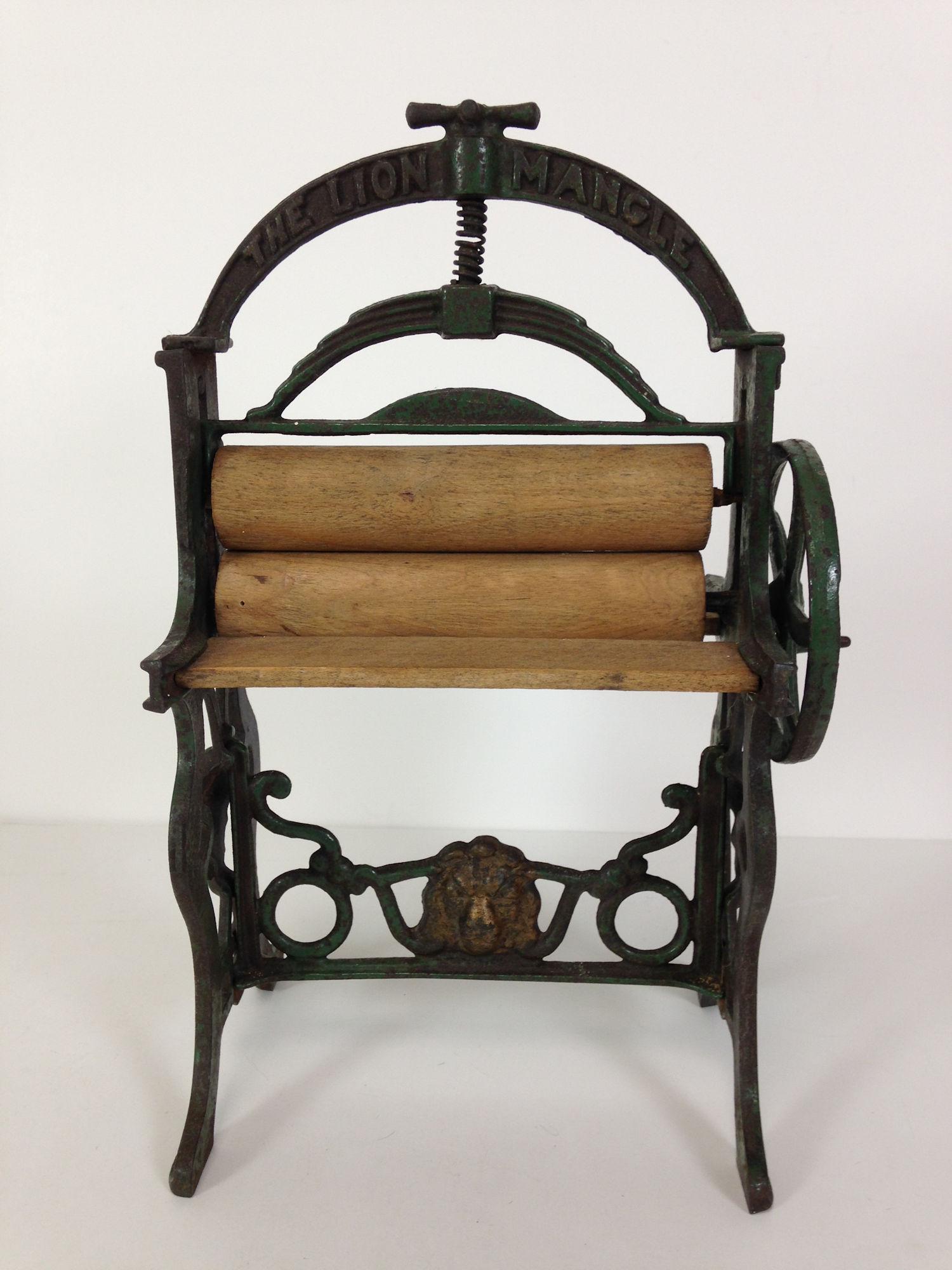 10 1/2" DOLLY SIZE MANGLE. PAINTED CAST IRON WITH WOOD: 10 1/2" DOLLY SIZE MANGLE. PAINTED CAST IRON WITH WOOD ROLLERS AND PLATFORM, WORKING WHEEL. EMBOSSED LION'S HEAD AT BOTTOM AND "THE LION MANGLE" AT THE TOP.