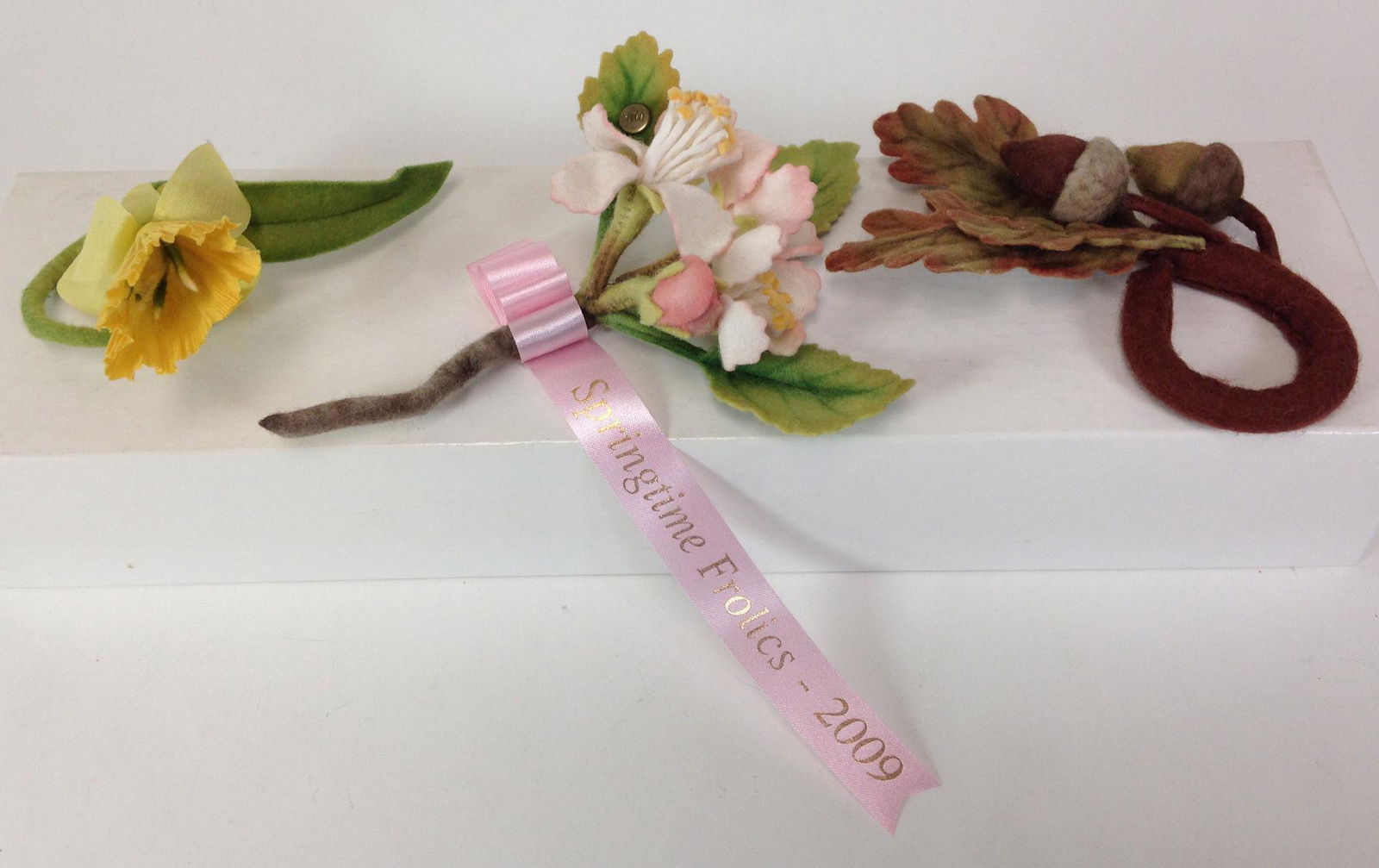 (3) R. JOHN WRIGHT UFDC CONVENTION SOUVENIRS INCLUDING: (3) R. JOHN WRIGHT UFDC CONVENTION SOUVENIRS INCLUDING APPLE BLOSSOM CORSAGE, DAFFODIL NAPKIN RING AND ACORN NAPKIN RING.