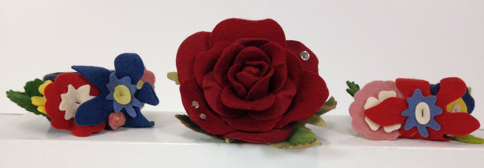 (3) R. JOHN WRIGHT NAPKIN RINGS MADE FOR UFDC: (3) R. JOHN WRIGHT NAPKIN RINGS MADE FOR UFDC CONVENTIONS INCLUDING (2) 2004 "MAGICAL HOUR" NAVY AND LIGHT BLUE ALL FELT WITH APPLIED FLOWERS AND (1) 2010 "RAINDROPS ON ROSES" DEEP RED ALL FELT WITH A