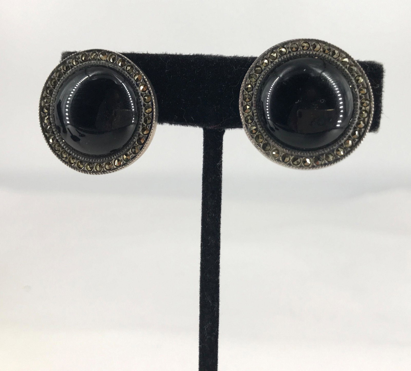 VINTAGE SILVER AND MARCASITE EARRINGS: VINTAGE SILVER AND MARCASITE EARRINGS ~ HINGED CLOSURES. STAMPED STERLING BUT TEST AS 70% SILVER. 0.565 TROY OUNCES TW. 1" IN DIAMETER. POLISHED BLACK ONYX CENTER STONE CABOCHONS IN MARCASITE HALOS.