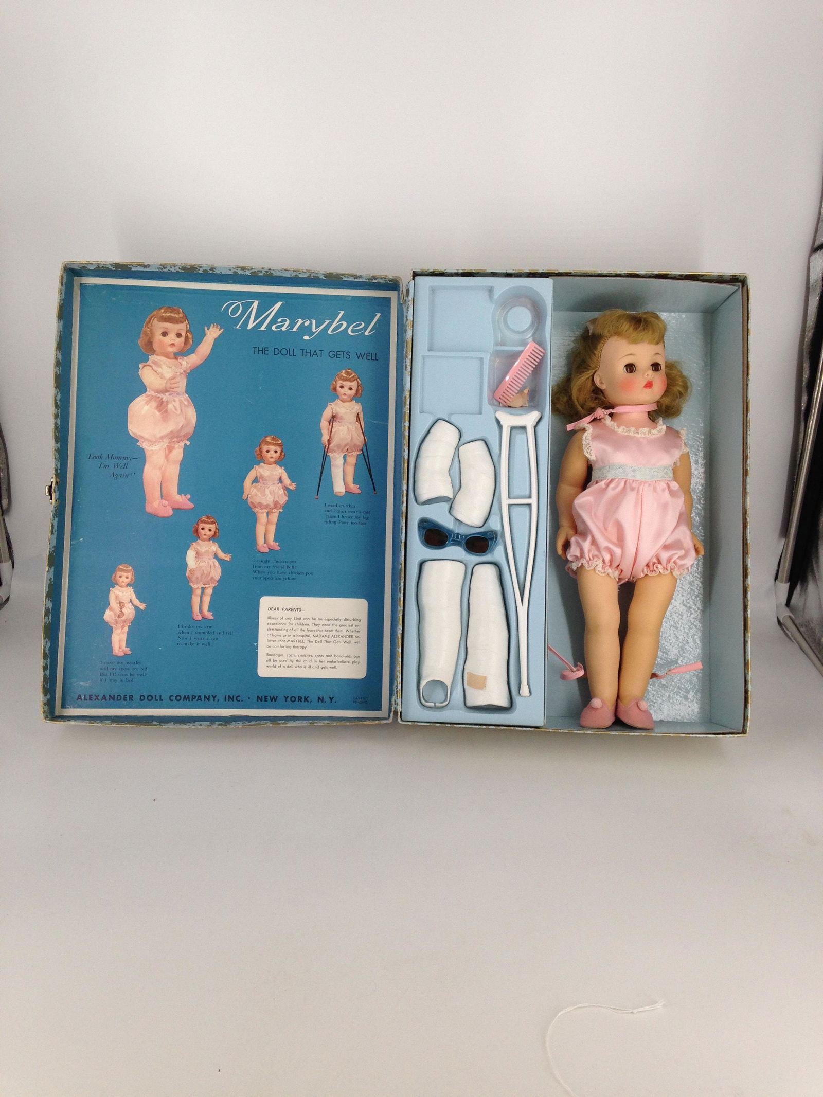16" VINTAGE MADAME ALEXANDER "MARYBEL THE DOLL THAT: 16" VINTAGE MADAME ALEXANDER "MARYBEL THE DOLL THAT GETS WELL" IN ORIGINAL CASE. VINYL SOCKET HEAD WITH ROOTED BLONDE HAIR AND SLEEP EYES. WEARS ORIGINAL ONE-PIECE PINK SATIN SUIT AND PINK SHOES WITH