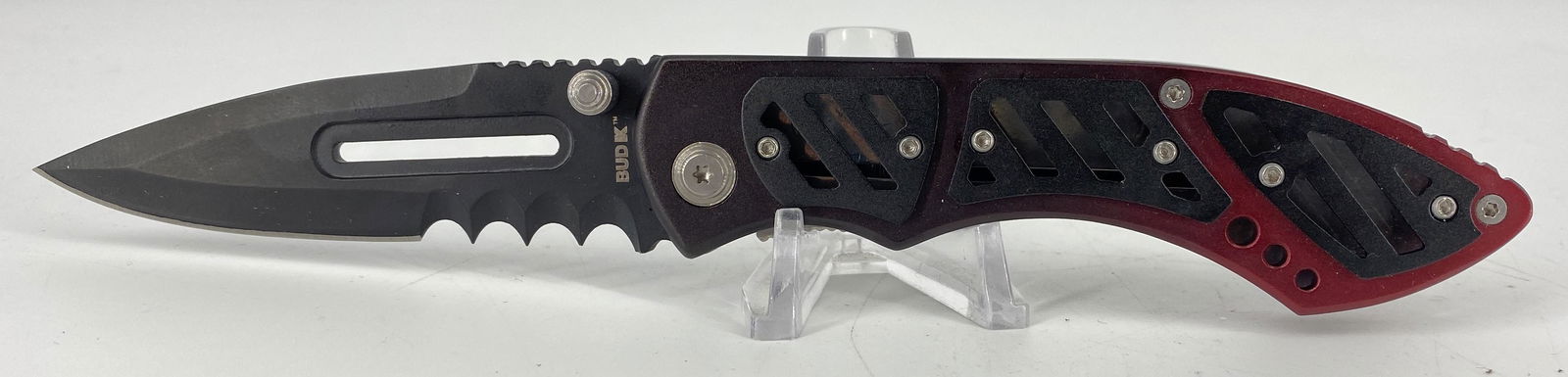Folding Knife: Folding Knife 8.125” in total length, drip point blade with a deep ridged saw blade near the hinge, ombrÃ© black-red handle with openwork black metal scales, crafted by BUD K, #BK112020, openw