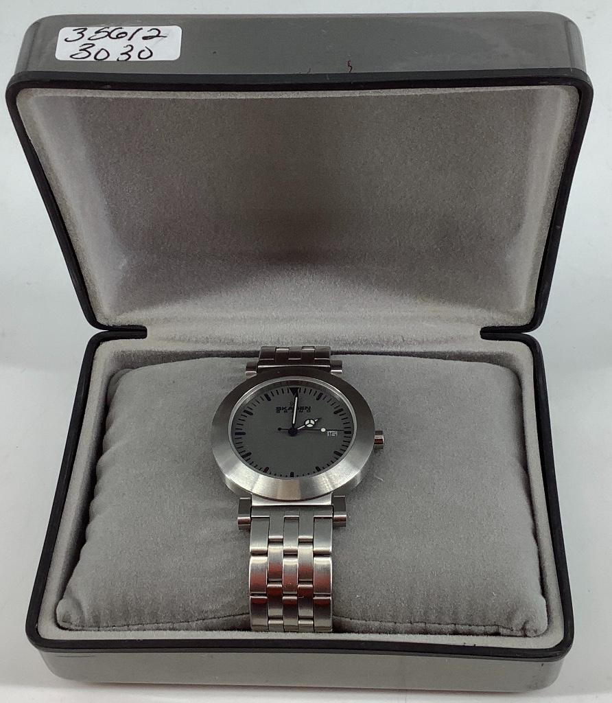 Skagen Wrist Watch: Skagen Wrist Watch New old stock with manual, silver tone base metal band and bezel, grey face with black stick numeric indicators, watch winds, sets and ticks at time of listing serial #128LSX