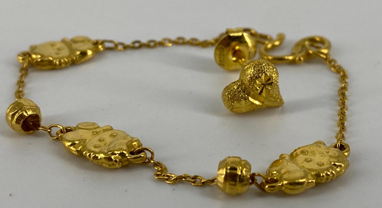 One High Kt Gold Earring & One High Kt Gold Childs: One High Kt Gold Earring & One High Kt Gold Childs Bracelet Post back earring features a heart shaped motif with a textured finish, tests as 22kt+ & one 5.5Ã® Childs charm bracelet that features Hel