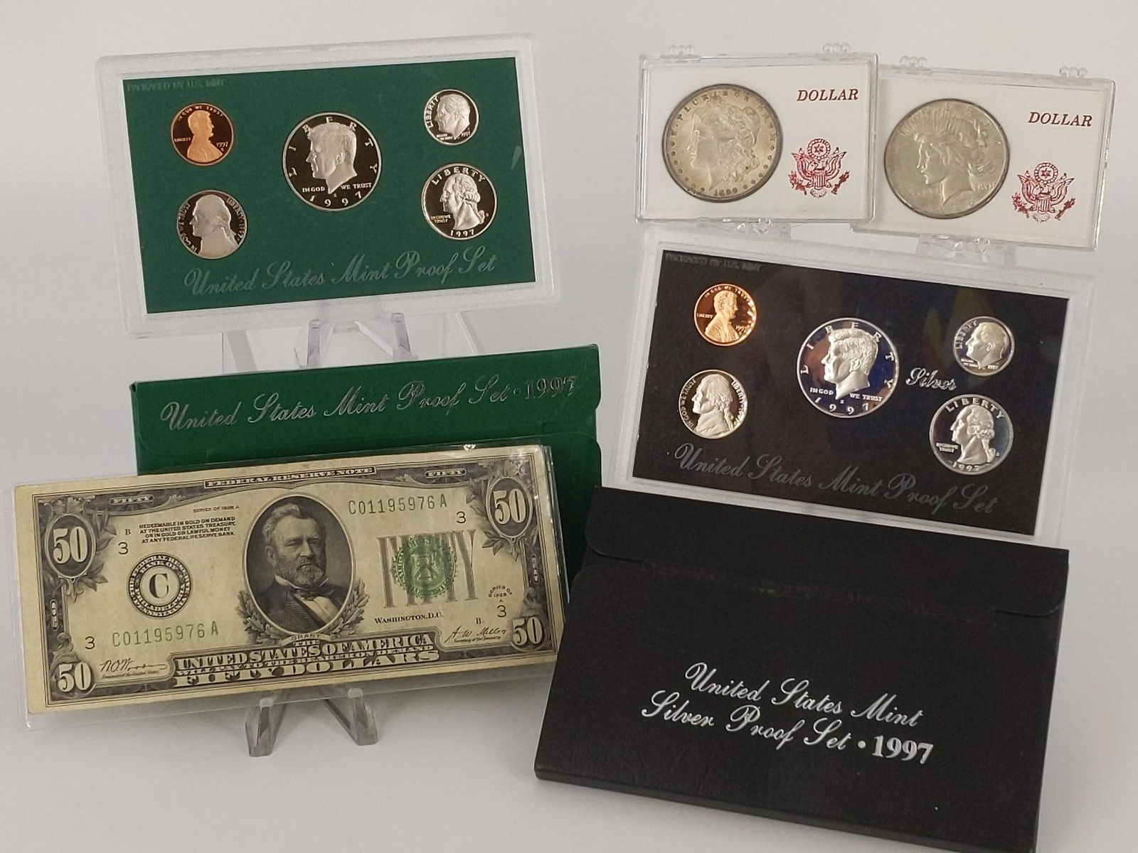 Two Proof/Mint Sets and Two U.S. Silver Dollar Coins +: Two Proof/Mint Sets and Two U.S. Silver Dollar Coins + Bill Two U.S. silver (90%) dollar coins in plastic cases dated 1899-O (Morgan) and 1926 (Peace). Not professionally graded coins. One 1928A U.S.