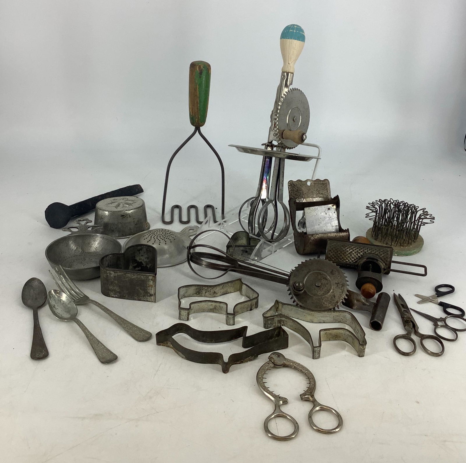 Lot of vintage metal kitchen tools including Victorian: Lot of vintage metal kitchen tools including Victorian egg topper/cutter, 2 hand beaters, 1 grater, 4 cookie cutters, green handled masher,metal railroad spike and several other pieces Total of 21 pie