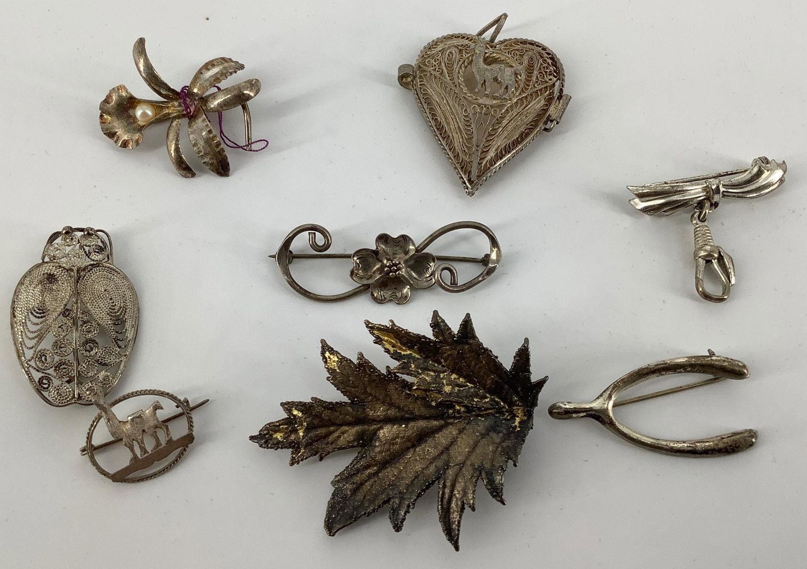 Seven Sterling Silver Pins and Locket: The pieces feature leaves, wire work, floral, bar guard, wishbone, lama. Ranging in size from .75" to 2" in length. Weighting 0.944 ozt