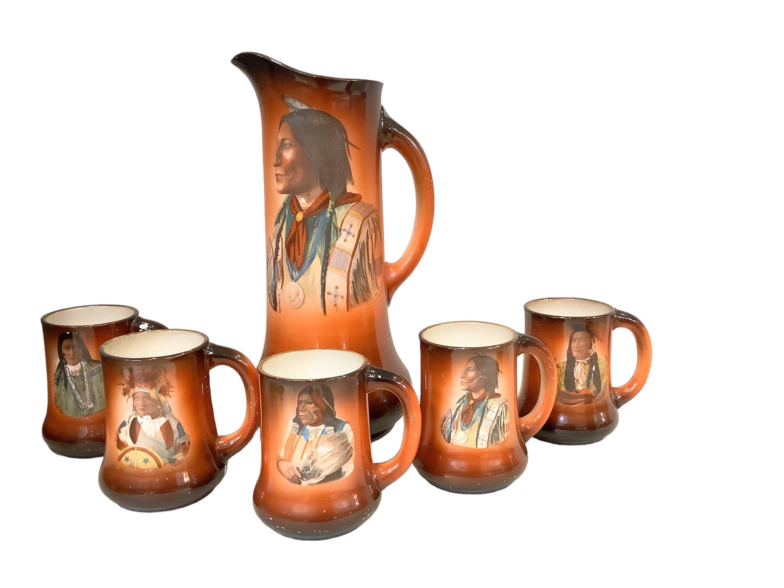 Tall Pitcher & Mugs with American Indian Motif: Tall Pitcher & Mugs with American Indian Motif This 14"H pitcher and (5) mugs are each decorated with an image of a different American Indian. Paint has chipped/flaked in several places. Made in China