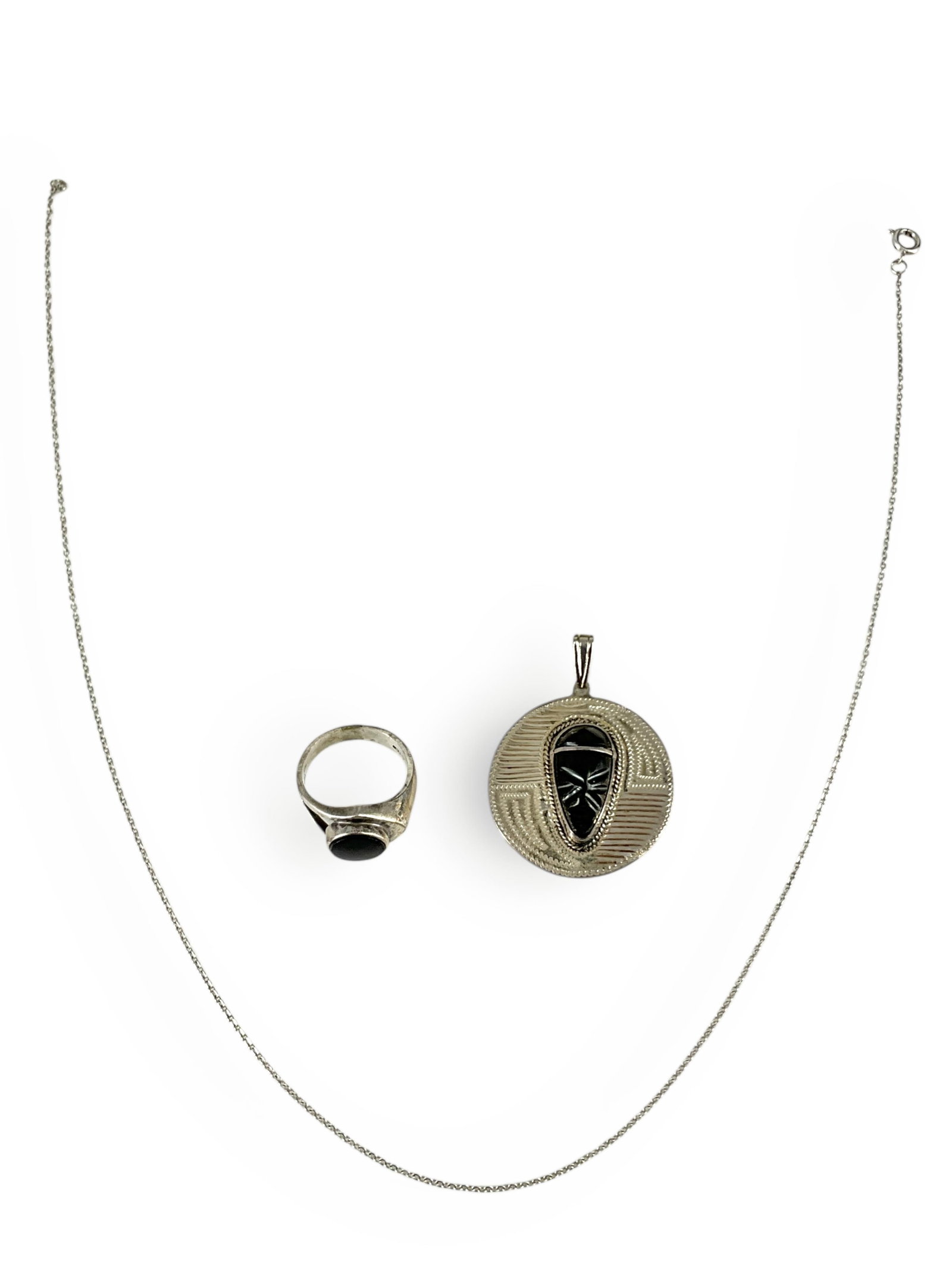 Silver Mask Pendant and Onyx Ring in Silver: Silver Mask Pendant and Onyx Ring in Silver Pendant is created in tested silver, front of round-shaped pendant holds a bezel-set, carved black mask (likely of onyx) on an etched silver background, the