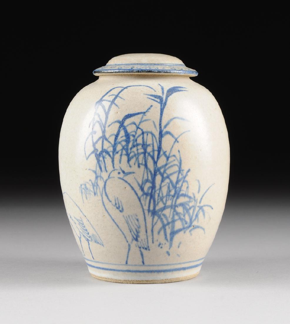 A MODERN COBALT BLUE DECORATED BUFF GLAZED EARTHENWARE: A MODERN COBALT BLUE DECORATED BUFF GLAZED EARTHENWARE LIDDED JAR, INCISED SQUARE FORM ARTIST'S SIGNATURE, of ovoid form and sides centering birds foraging amongst tall marsh foliage, surmounted by a 