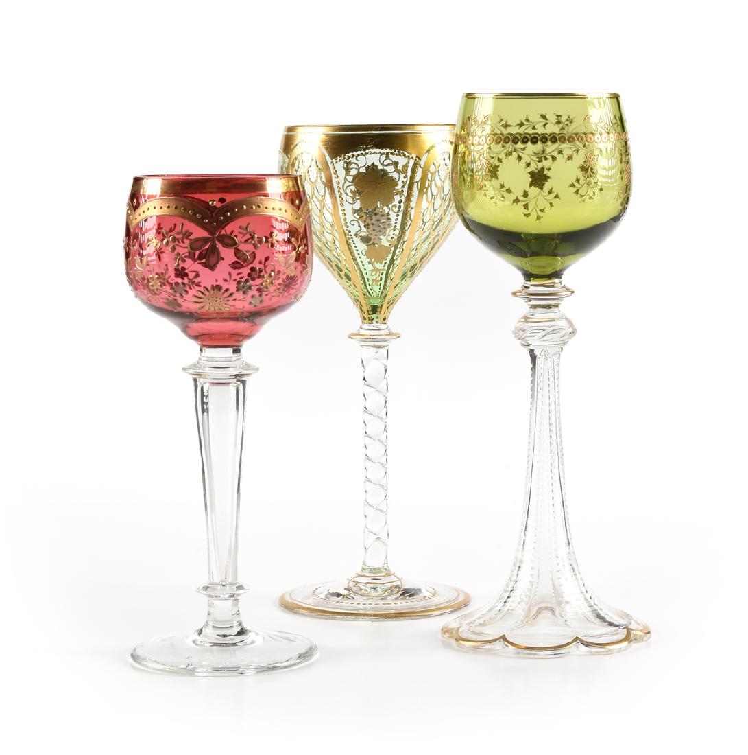 A GROUP OF THREE BOHEMIAN WINE STEMS,: A GROUP OF THREE BOHEMIAN WINE STEMS, comprising a wine glass with cranberry glass bowl decorated in gilt with beaded arches over raised floral sprays, over a clear tapering columnar hollow shaft stem
