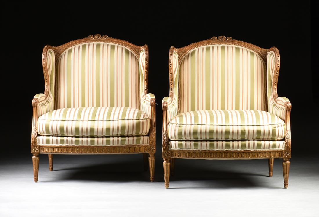 A PAIR OF LOUIS XVI STYLE PARCEL GILT BEECH BERGÈRE À: A PAIR OF LOUIS XVI STYLE PARCEL GILT BEECH BERGÈRE À OREILLES, EARLY 20TH CENTURY, the three flower blooms center an arched, molded crest rail with a central bead and acanthus repeating motif, over