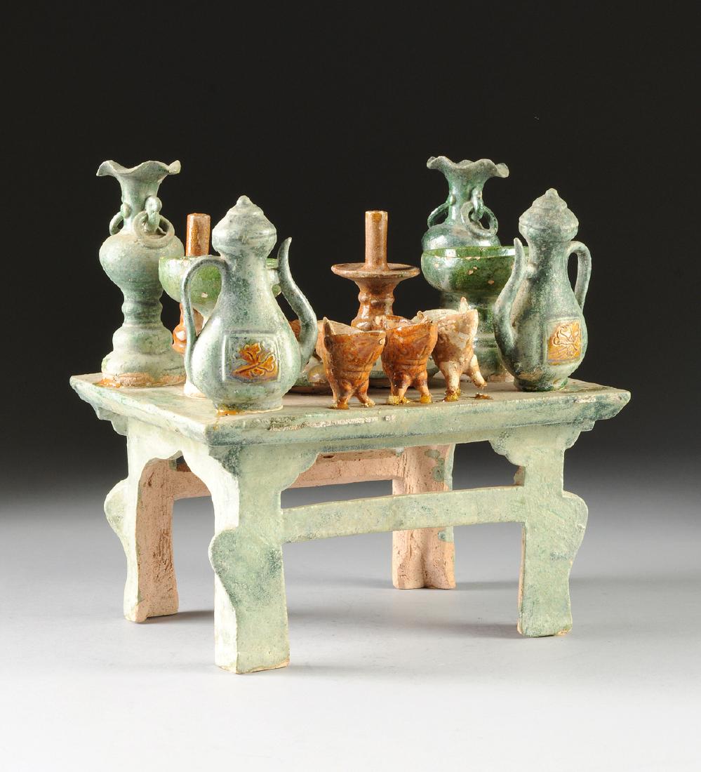 A SANCAI GLAZED AND BUFF POTTERY TOMB OFFERINGS TABLE,: A SANCAI GLAZED AND BUFF POTTERY TOMB OFFERINGS TABLE, POSSIBLY MING DYNASTY, CIRCA AD 1560, the rectangular green buff table mounted with various vessels and wares including a covered wine ewer, cand