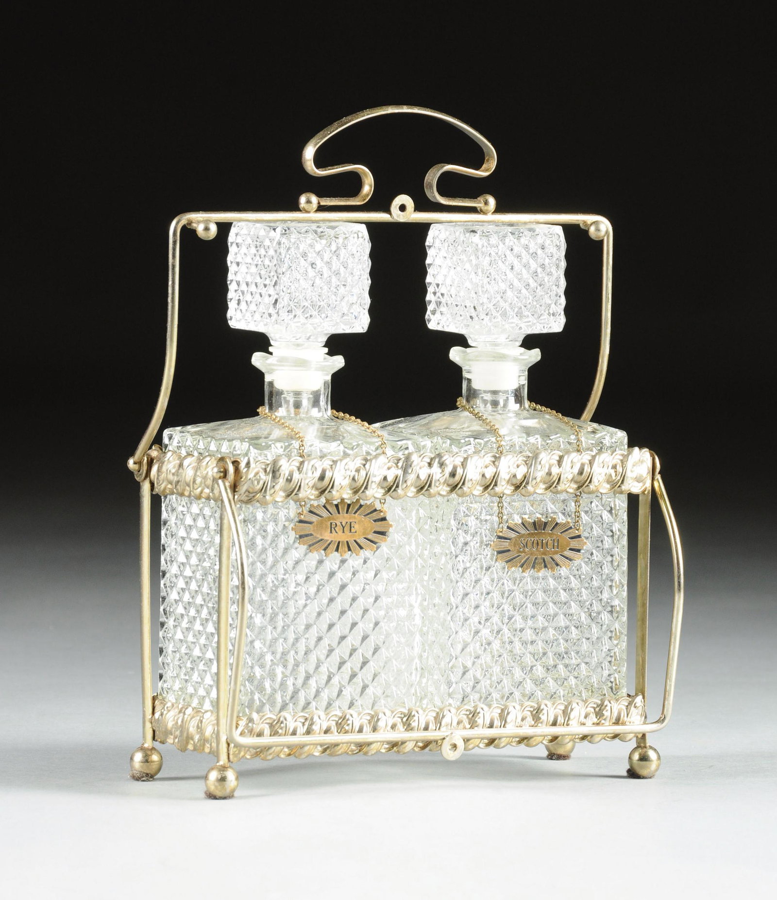 AN AMERICAN GLASS AND SILVER PLATE TWO BOTTLE LIQUOR: AN AMERICAN GLASS AND SILVER PLATE TWO BOTTLE LIQUOR TANTALUS, EARLY 20TH CENTURY, the silver plate frame of exposed rod construction with pressed rope form bands with alternating egg and leaf decorat