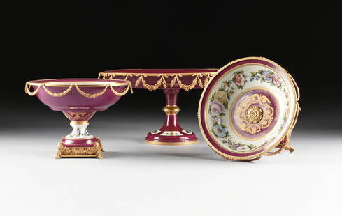 A BELLE ÉPOQUE THREE PIECE GILT METAL MOUNTED PORCELAIN: A BELLE ÉPOQUE THREE PIECE GILT METAL MOUNTED PORCELAIN CENTERPIECE AND TAZZAS, GERMAN, FIRST HALF 20TH CENTURY, in the Vienna style, with gilt decorated crimson ground bordered by wide reserved