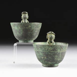 A GROUP OF TWO CHINESE ARCHAISTIC STYLE BRONZE: A GROUP OF TWO CHINESE ARCHAISTIC STYLE BRONZE "SURPRISE" OR "TRICK" CUPS,each of tapering circular form and exterior rim of continuous scrolls banding, enclosing an interior standing bearded Immortal