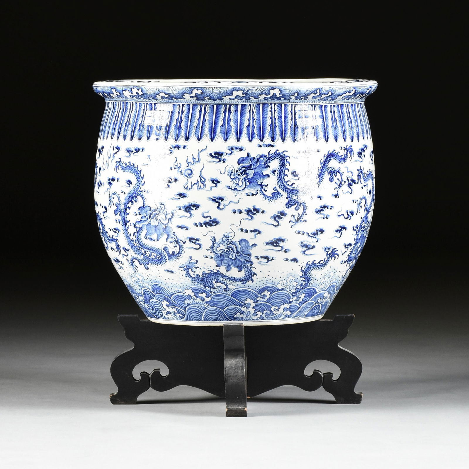 A CHINESE BLUE AND WHITE PORCELAIN JARDINIÃˆRE, DRAGON: A CHINESE BLUE AND WHITE PORCELAIN JARDINIÃˆRE, DRAGON IN THE CLOUDS, MODERN, of shaped bud form with a flat rim centering bloom and curling stems decoration, above a shoulder of exotic long leaf ba