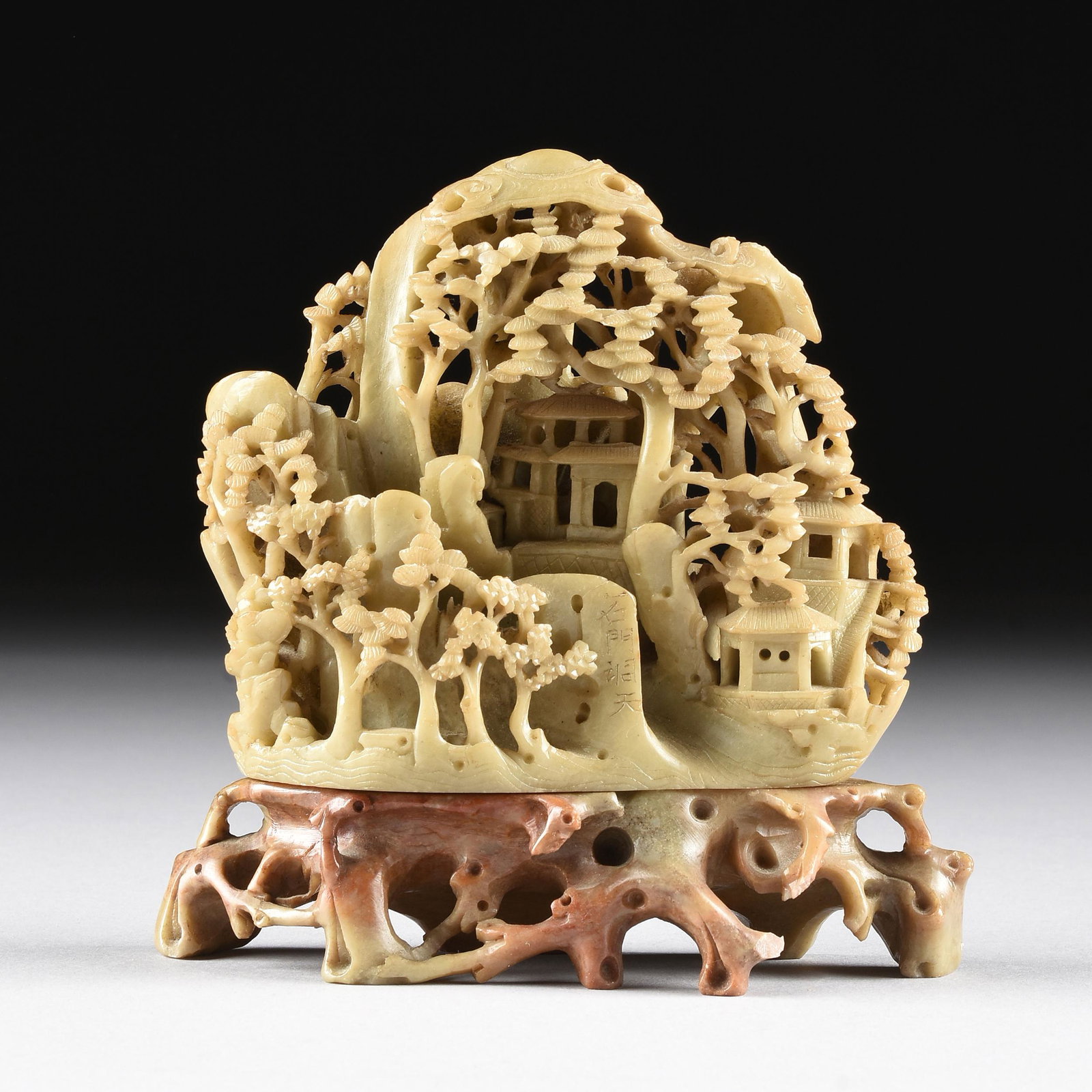 A CHINESE SOAPSTONE RETICULATED CARVING AND STAND, LATE: A CHINESE SOAPSTONE RETICULATED CARVING AND STAND, LATE 20TH CENTURY, modeled as a flat backed boulder of rocky mountainside pavilions and structures beneath the branches of tall ancient pines with ch