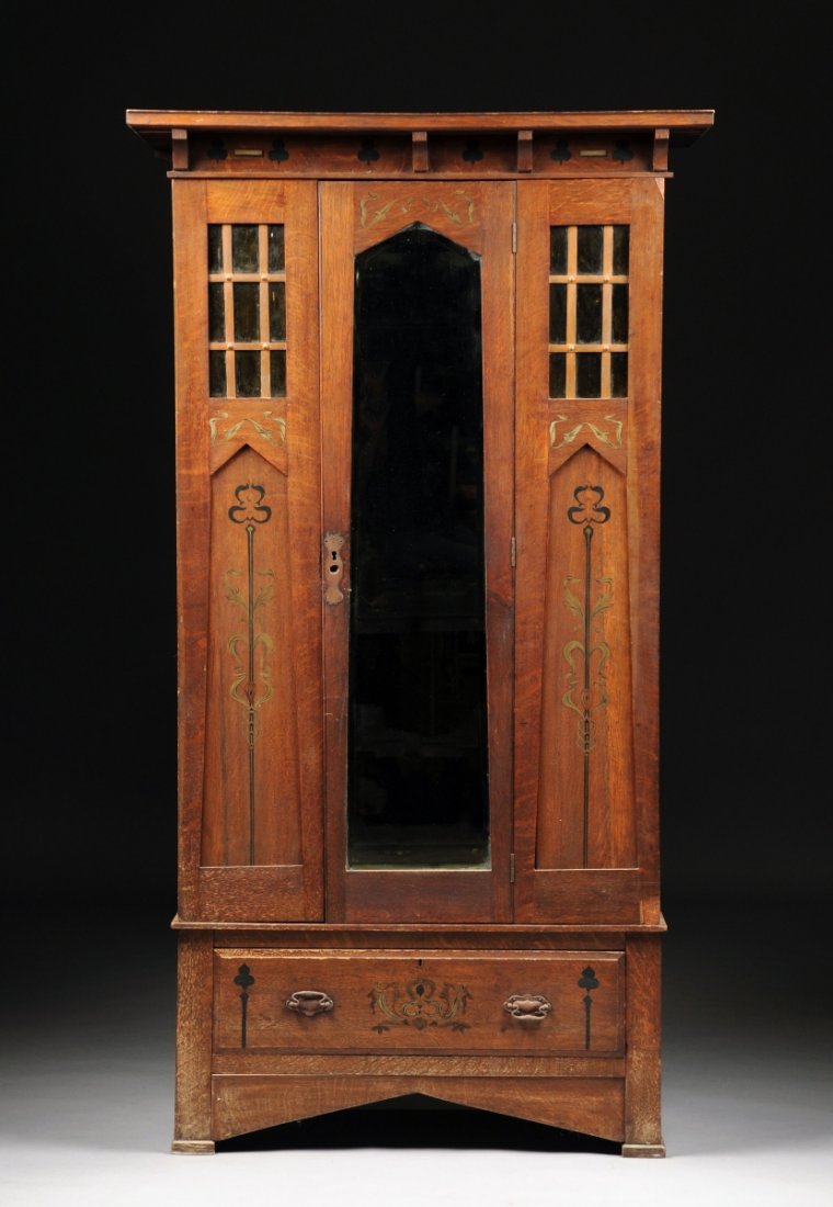 AN ENGLISH ARTS & CRAFTS OAK ARMOIRE, EARLY 20TH: AN ENGLISH ARTS & CRAFTS OAK ARMOIRE, EARLY 20TH CENTURY, the rectangular cornice above a frieze of black painted shamrocks alternating shaped brackets, on a pylon shaped case centering a conforming d