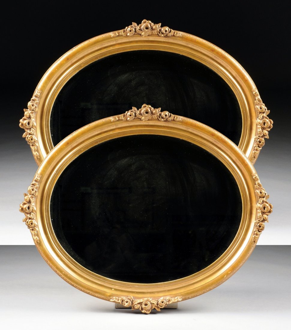A PAIR OF GILTWOOD OVAL MIRRORS, 19TH/20TH CENTURY,: A PAIR OF GILTWOOD OVAL MIRRORS, 19TH/20TH CENTURY, the beveled oval frame with rose and ribbon adornments in front of an egg and dart trim. Height: 29" Width: 35"