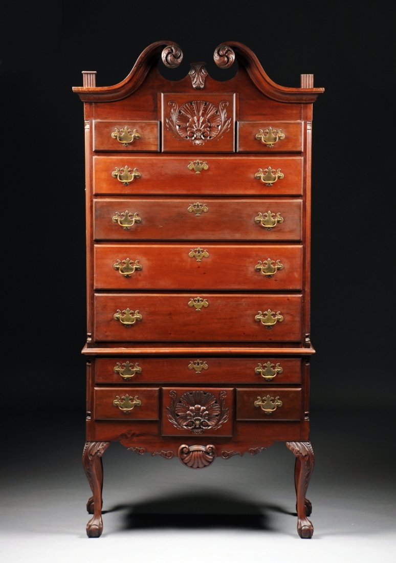 AN AMERICAN CHIPPENDALE STYLE CARVED MAHOGANY HIGHBOY,: AN AMERICAN CHIPPENDALE STYLE CARVED MAHOGANY HIGHBOY, the scrolled broken arched pediment separated by three urn form flaming finials, above a central shell carved drawer, flanked by two short drawer