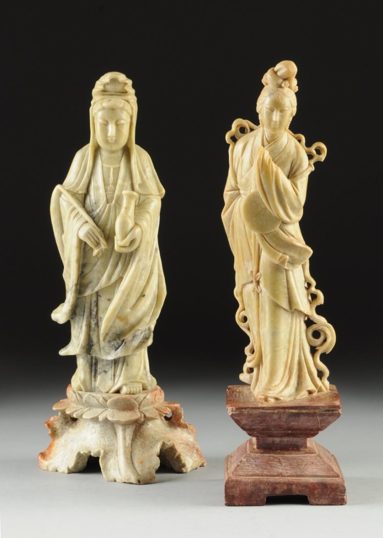 TWO CARVED SOAPSTONE FIGURES OF GUANYIN, 20TH CENTURY,: TWO CARVED SOAPSTONE FIGURES OF GUANYIN, 20TH CENTURY, one styled as a man with flowing robes, holding scholars items in his hands, standing on open petaled lotus base supported by a foot carved as a 