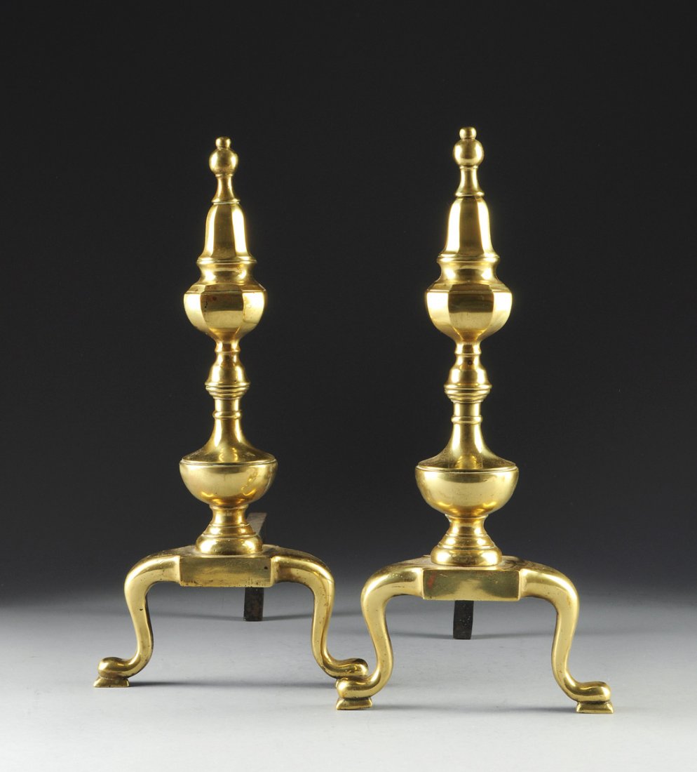 A PAIR OF BRASS ANDIRONS, EARLY 20TH CENTURY,: A PAIR OF BRASS ANDIRONS, EARLY 20TH CENTURY, the waisted and turned brass andirons supported by two out turned pad feet. Height: 17 1/2" Width: 9" Depth: 13"