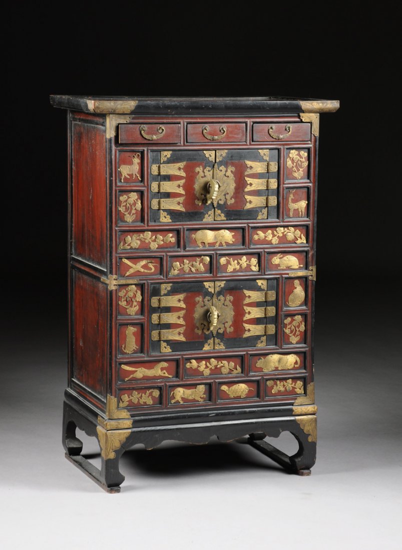 AN ANTIQUE KOREAN BRASS MOUNTED RED AND BLACK PAINTED: AN ANTIQUE KOREAN BRASS MOUNTED RED AND BLACK PAINTED PAULONIA WOOD BRIDAL CHEST-ON-STAND, CIRCA 1900, the rectangular top above three short drawers over two pairs of cabinet doors, enclosed by sham d
