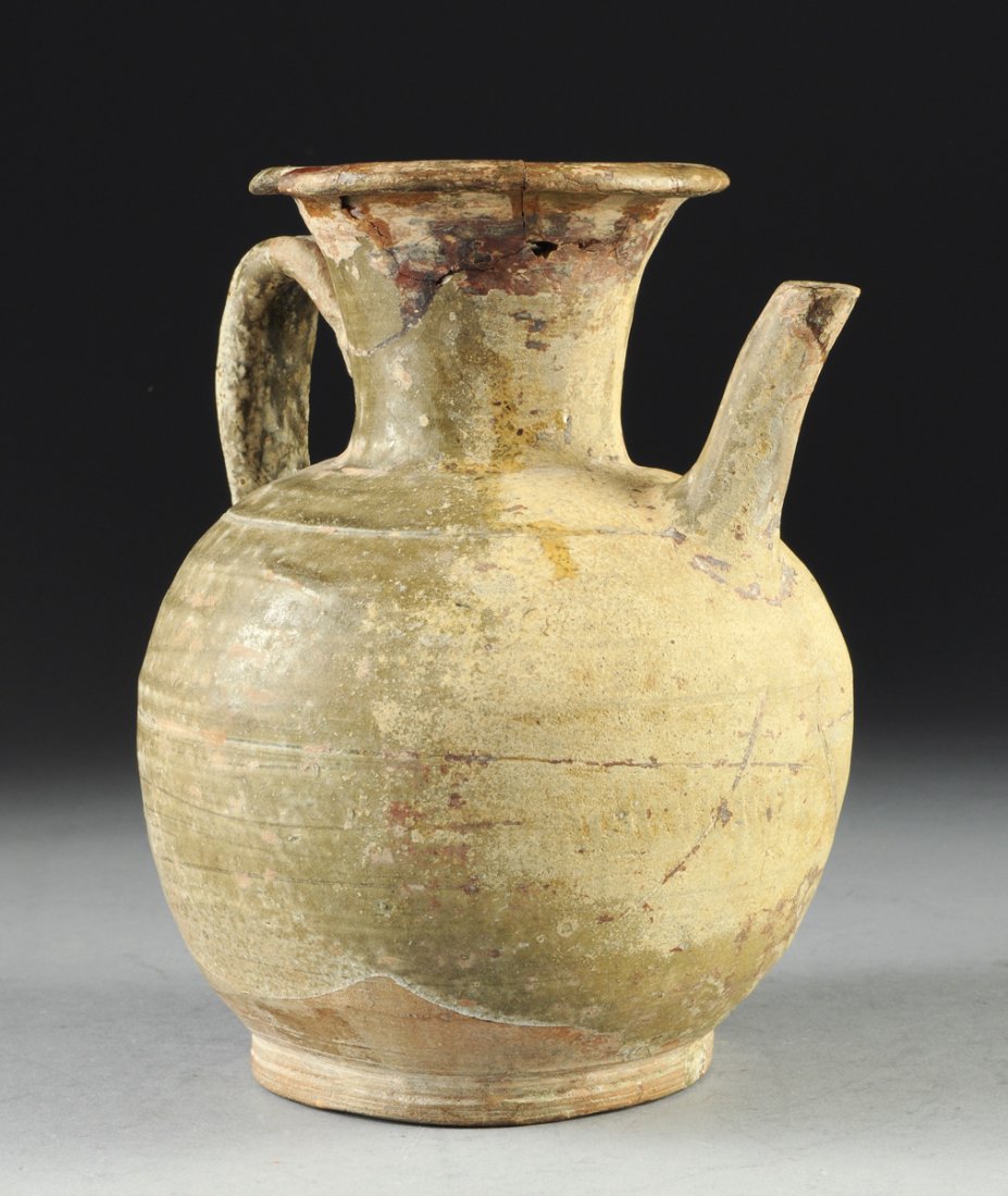 AN ANCIENT HAN DYNASTY CHINESE EWER WITH GLOBULAR BODY: AN ANCIENT HAN DYNASTY CHINESE EWER WITH GLOBULAR BODY AND FLARED SCROLLED POURING SPOUT, CIRCA 200 B.C. - 220 A.D., the neck and body joined with loop handle, the green glaze falling irregularly to t