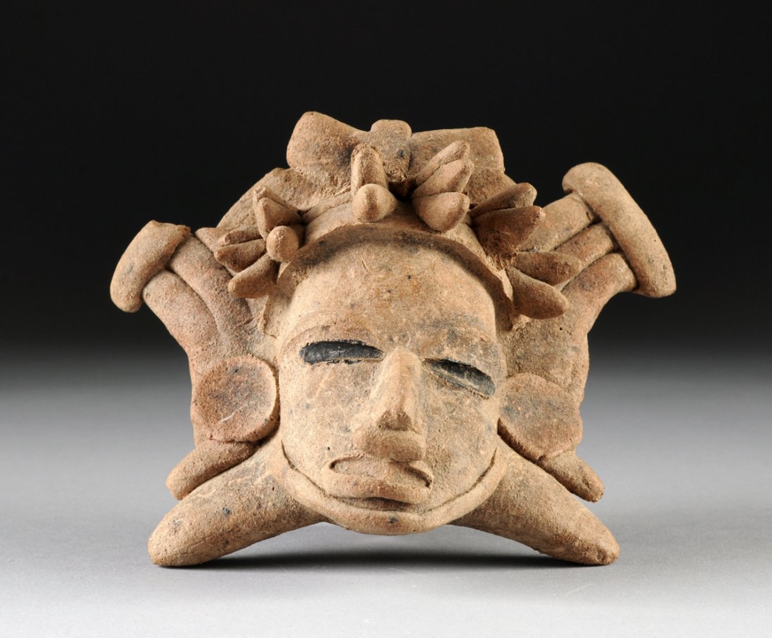 A PRE-COLUMBIAN MAYAN BAKED CLAY OCARINA,: A PRE-COLUMBIAN MAYAN BAKED CLAY OCARINA, modeled as a deity head wearing an elaborate headdress and large disc earrings flanking a stylized expression with blackened eyes on splayed supports reversin