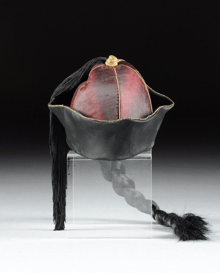 A CHINESE IRIDESCENT RED AND BLACK SILK WINTER HAT WITH: A CHINESE IRIDESCENT RED AND BLACK SILK WINTER HAT WITH A LADY'S POLYCHROME SILK NEEDLEWORK PLUM GROUND SKIRT, POSSIBLY LATE QING DYNASTY AND REPUBLIC PERIODS, , of domed circular form with an upturne