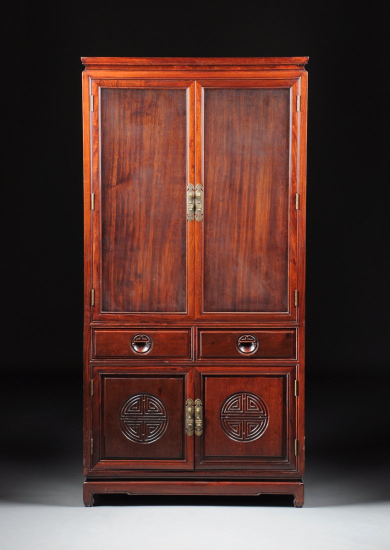 A CHINESE CARVED HARDWOOD DISPLAY CABINET, MODERN,: A CHINESE CARVED HARDWOOD DISPLAY CABINET, MODERN, the rectangular cornice above two glazed doors and two short drawers with recessed circular handles, over paneled doors enclosing circular archaistic