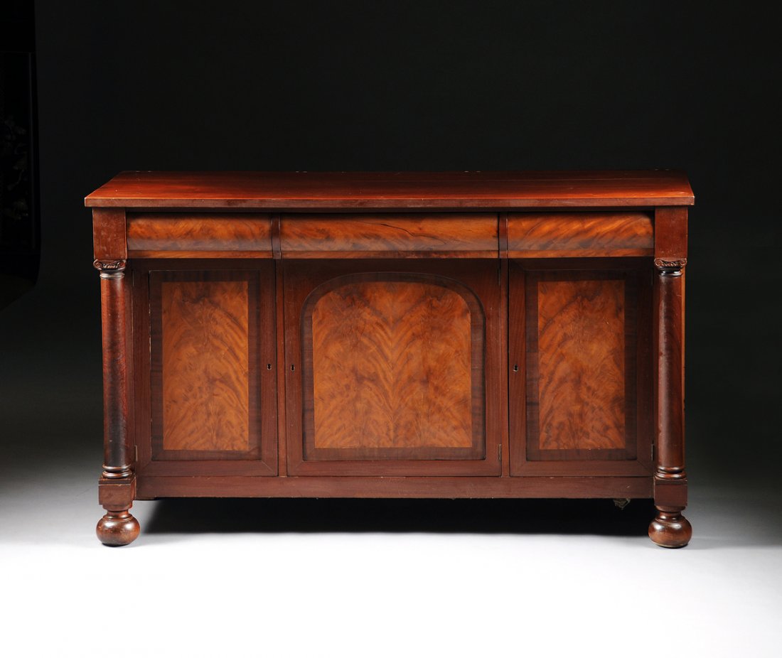 AN AMERICAN CLASSICAL CARVED MAHOGANY SIDEBOARD, SECOND: AN AMERICAN CLASSICAL CARVED MAHOGANY SIDEBOARD, SECOND QUARTER 19TH CENTURY, the rectangular top above three frieze drawers with rounded faces over a central hinged door with cross-banded and arched 