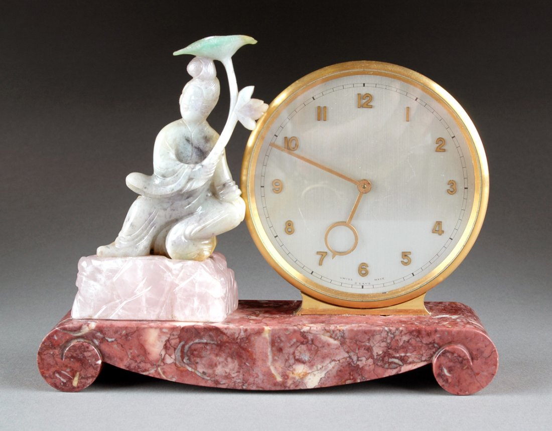 AN ART DECO CARVED HARDSTONE FIGURAL MANTLE CLOCK,: AN ART DECO CARVED HARDSTONE FIGURAL MANTLE CLOCK, SECOND QUARTER 20TH CENTURY, the Chinese green jadeite figure of a maiden with lotus parasol on a rose quartz plinth flanking a gilt bronze glazed ci